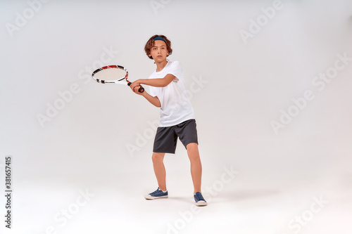 Playing tennis. Full-length shot of a teenage boy holding tennis racket and looking away isolated over grey background