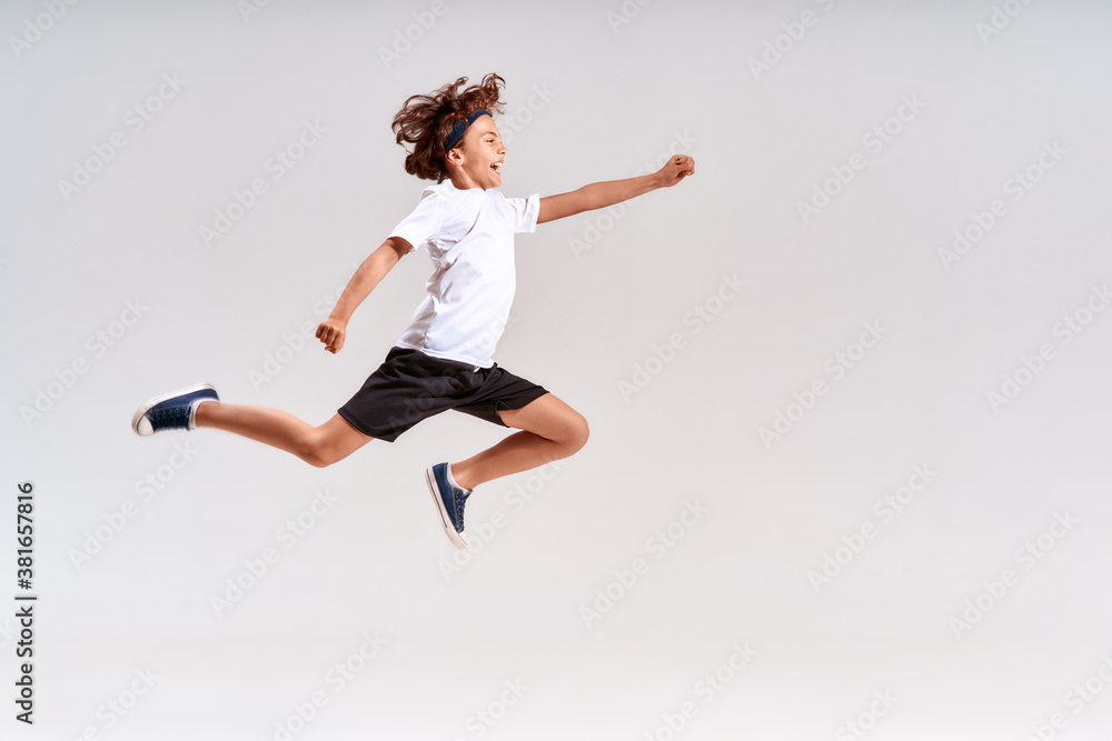 Children engaged in sport. Full-length shot of a teenage boy jumping isolated over grey background, studio shot