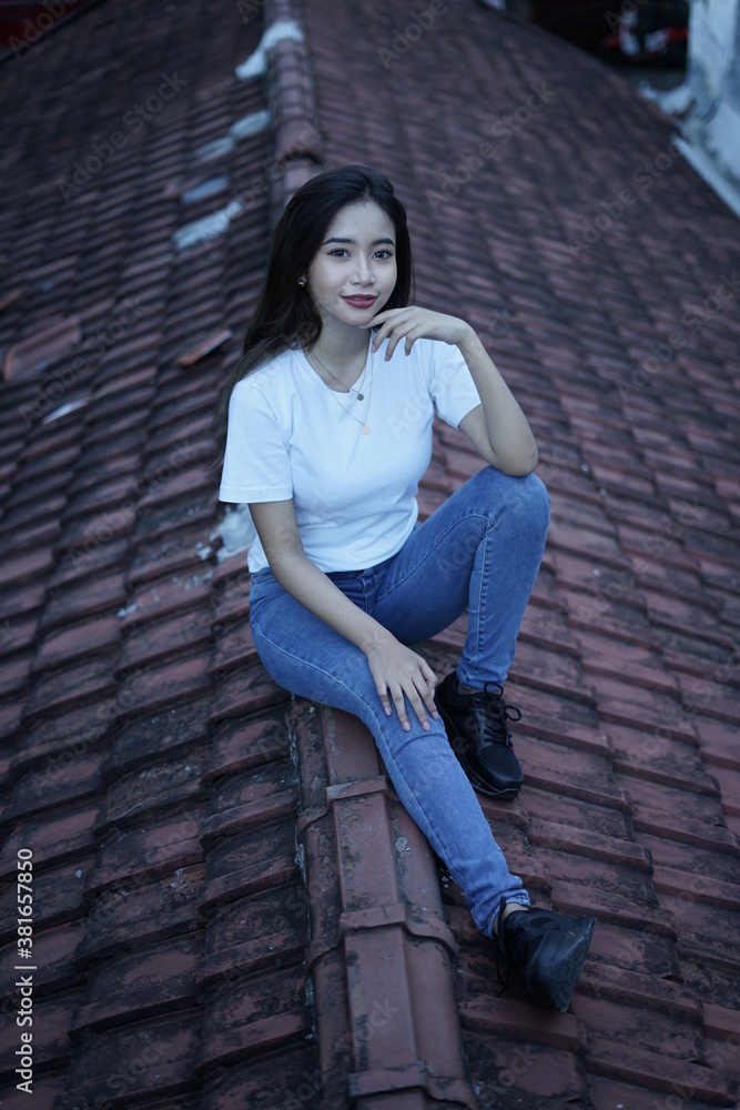 The blonde girl sits on the roof tile in a style wearing a white t-shirt. female t-shirt models for mockups and templates. The blonde girl sits on the roof tile in a style wearing a white t-shirt. female t-shirt models for mockups and templates.
