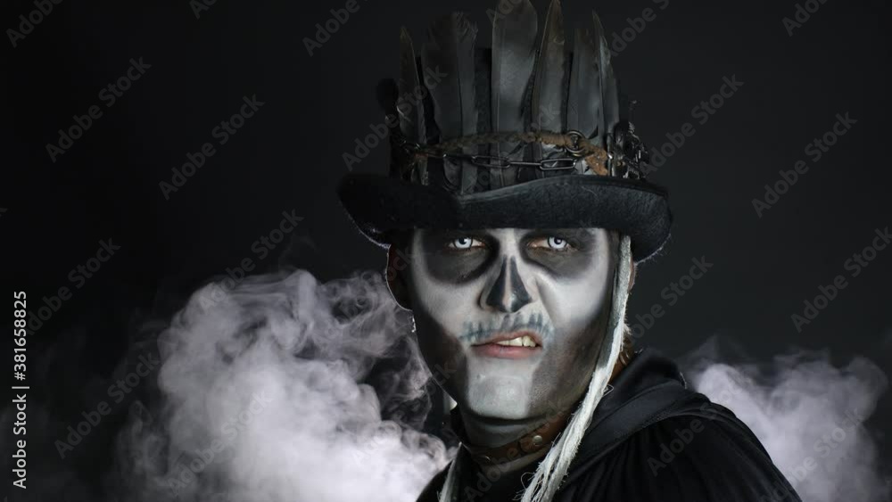 Sinister man with horrible Halloween skeleton makeup appearing from darkness when light falls on him Sinister man with horrible Halloween skeleton makeup appearing from darkness when light falls on him