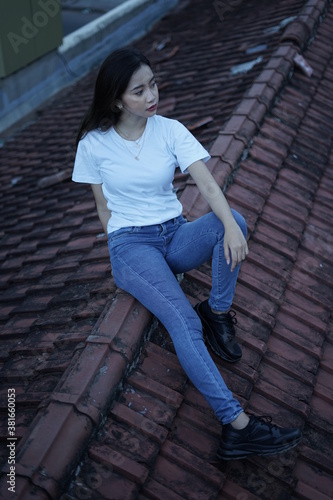 The blonde girl sits on the roof tile in a style wearing a white t-shirt. female t-shirt models for mockups and templates. © AndhikaRaya