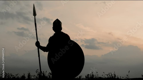 Silhouette of man in armour posing with spear in field.