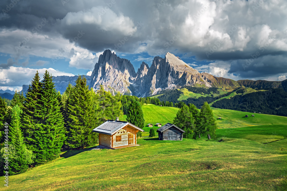 Famous Alpe di Siusi - Seiser Alm with Sassolungo - Langkofel mountain group in background at sunset. Wooden chalets in Dolomites, Trentino Alto Adige region, South Tyrol, Italy