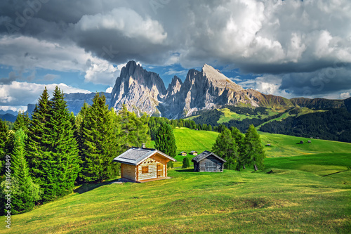 Famous Alpe di Siusi - Seiser Alm with Sassolungo - Langkofel mountain group in background at sunset. Wooden chalets in Dolomites, Trentino Alto Adige region, South Tyrol, Italy