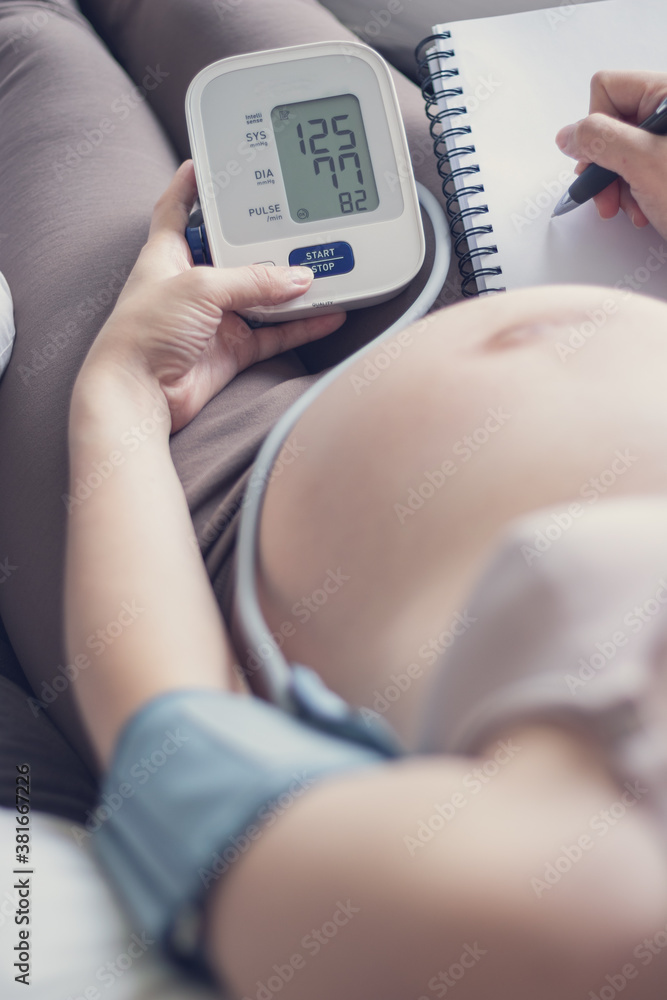 Pregnant woman measuring blood pressure at home, health check of expecting mom Pregnant woman measuring blood pressure at home, health check of expecting mom
