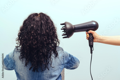 Woman styling her curly hair with hairdryer with special diffuser nozzle.