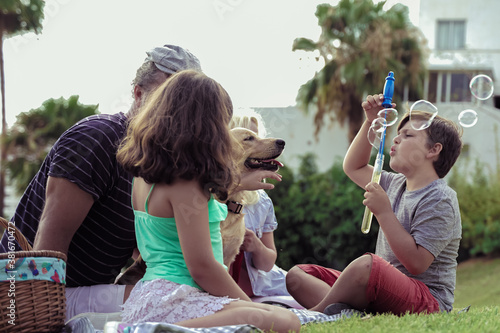 Happy family with their dog in a good sun day. The boy playing with soap bubbles. Happy family doing picnic in the park . Family and pet concept.