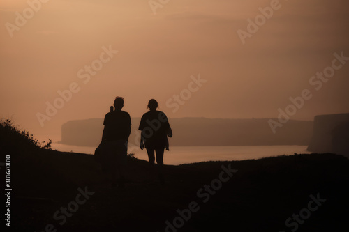 Silhouette of a couple walking into the sunset with seven sisters cliffs in the distance