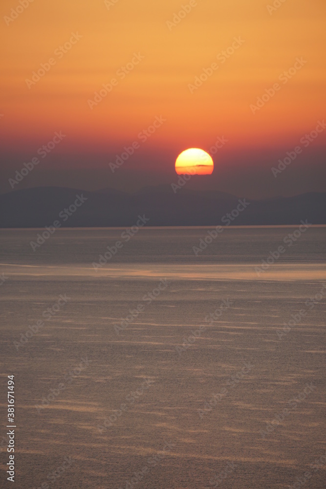 Die Sonne versinkt hinter den Wolken und Bergen am Meer Die Sonne versinkt hinter den Wolken und Bergen am Meer