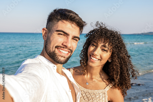 Картината върху платно Beautiful mixed race couple taking a selfie at the sea at dusk - Handsome young