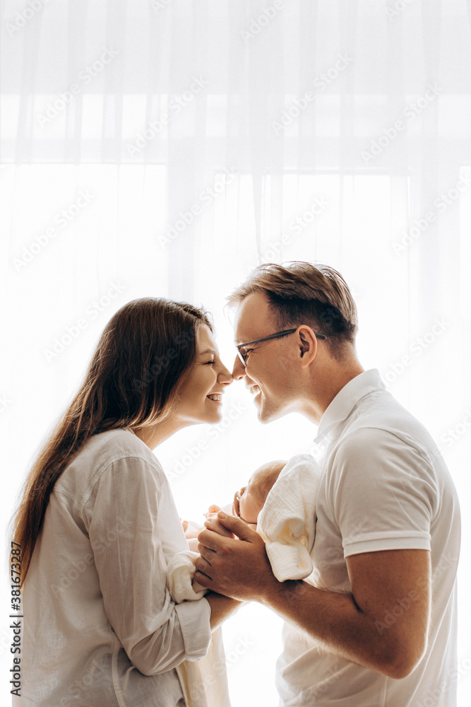 Lovely parents with newborn baby, loving mom hold little daughter in arms, caring dad hold hand of adorable baby girl, happy mother and father touch with noses, parenting concept Lovely parents with newborn baby, loving mom hold little daughter in arms, caring dad hold hand of adorable baby girl, happy mother and father touch with noses, parenting concept