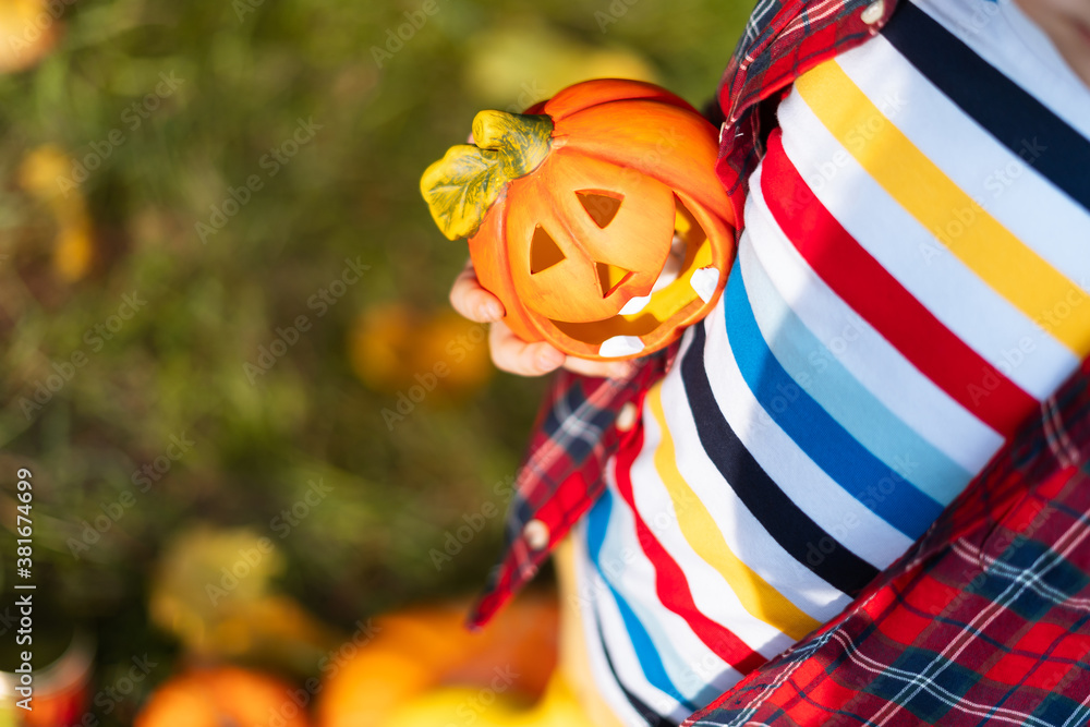Naklejka premium Kid's hand holding Jack'O pumpkin lamp, trick or treat on Halloween day. Concept for autumn holidays background