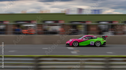 A panning shot of a pink and green racing car as it circuits a track.