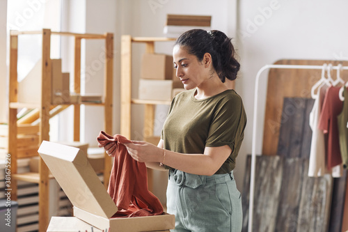 Young woman packing new shirt in cardboard box before delivering working in webstore