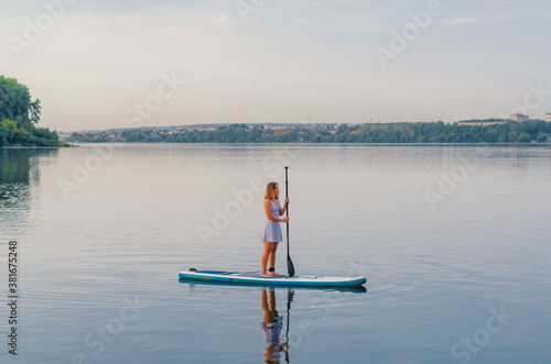 Woman in a dress on a sap board floats on the blue water of the