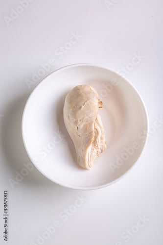 Boiled chicken breast fillet is in a white plate on a white background. View from above. Vertical orientation. High quality photo