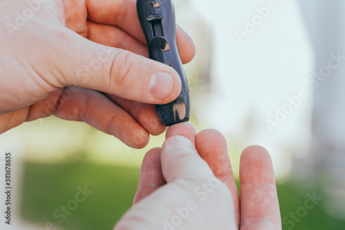 diabetes, glycemia, healthcare and people concept - close up of a man's hands using a lancet on his finger to check blood glucose meter