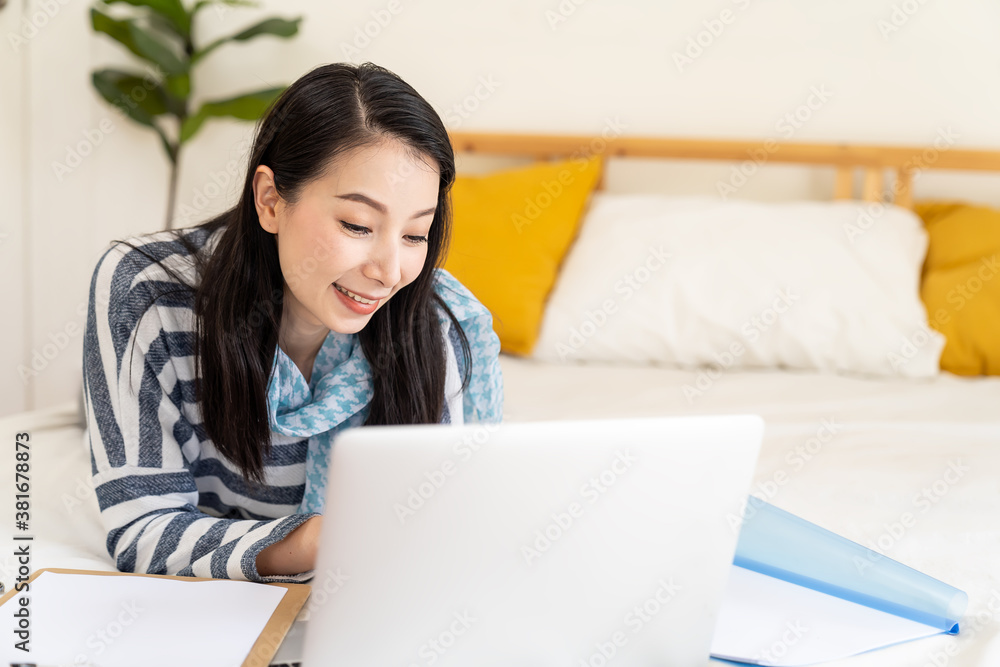 Happy young Asian woman using laptop computer on bed at home. Shopping online, Working from home, quarantined concept Happy young Asian woman using laptop computer on bed at home. Shopping online, Working from home, quarantined concept