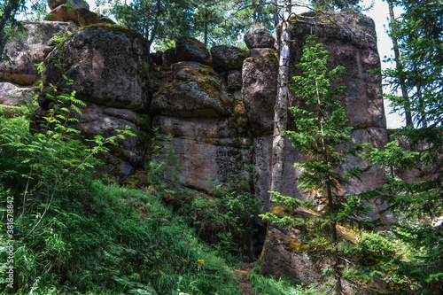 Geometric stone rocks covered with green moss in light of sun with shadows among coniferous trees forest. Cliff in nature park of Krasnoyarsk pillars