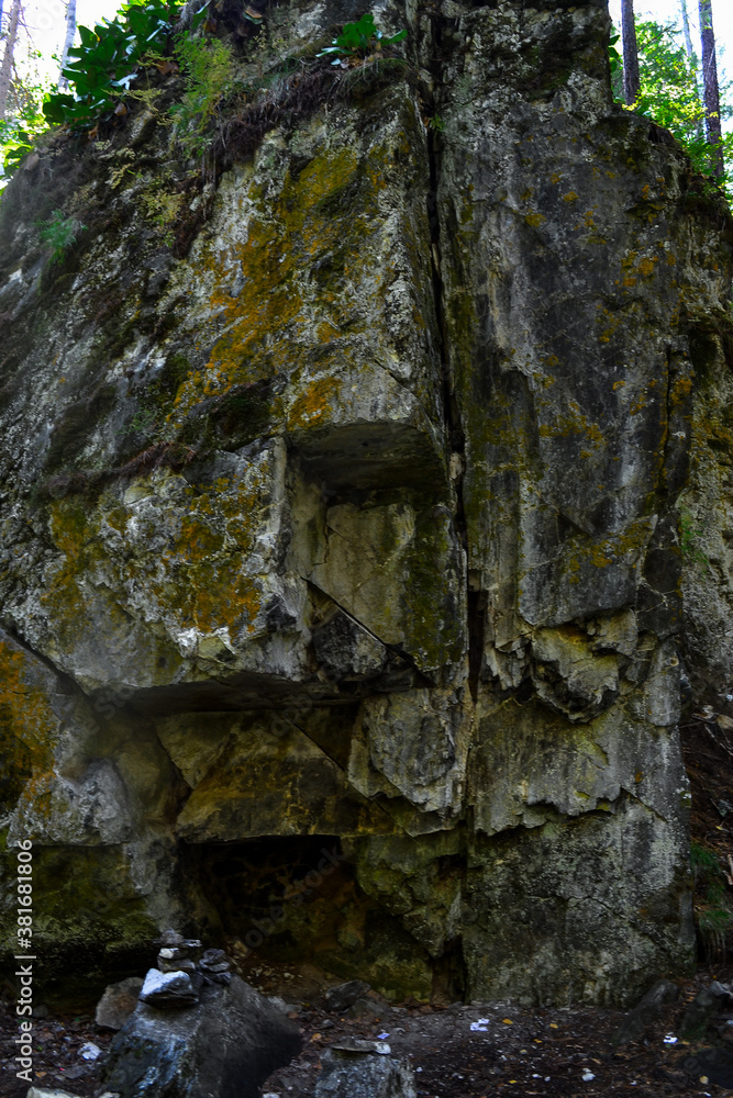 Big cliffs in forest. Large geometric rough stone rock overgrown with green moss in shadow, nature Big cliffs in forest. Large geometric rough stone rock overgrown with green moss in shadow, nature
