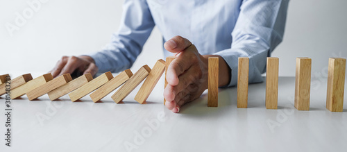 Risk and strategy in business, Close up of business woman hand stopping wooden block between three way from falling in the line of domino