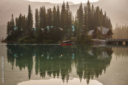 Fototapeta Naklejka Na Ścianę i Meble -  A red canoe moves over Emerald Lake in the morning with the surrounding reflected in the water (British Columbia, Canada)
