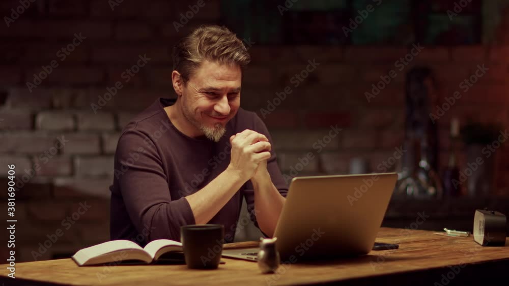Older man tele working with laptop computer at home office in dark room, typing and thinking, getting phone call, looking busy. Older man tele working with laptop computer at home office in dark room, typing and thinking, getting phone call, looking busy.