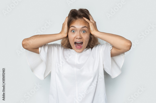 Blonde lady gesturing a headache screaming on a white studio wall wearing a shirt