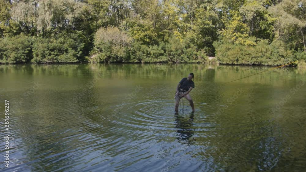 Caucasian man practicing slackline over the surface of the river in the forest. A man practices highlining over water in summer at dawn. Caucasian man practicing slackline over the surface of the river in the forest. A man practices highlining over water in summer at dawn.