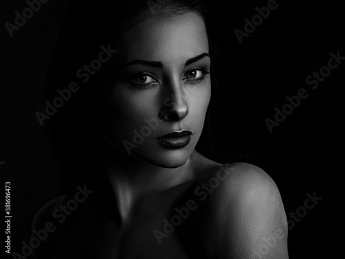 Beautiful mysterious woman in darkness looking dramatic on black background with empty copy space. Closeup portrait.