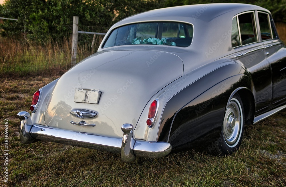 Rear view of classic, vintage car, two toned gray and black in a countryside setting with fading sunlight