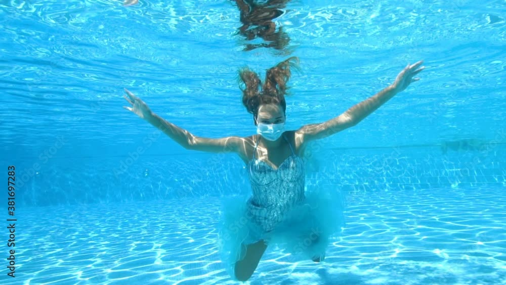 Conceptual portrait of a girl in a medical mask under water. She swims ...