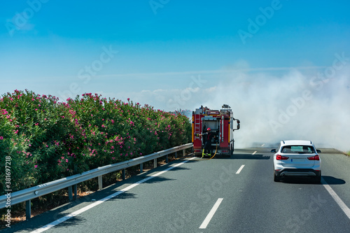 Fire truck putting out a fire in the bushes of the median of the highway.