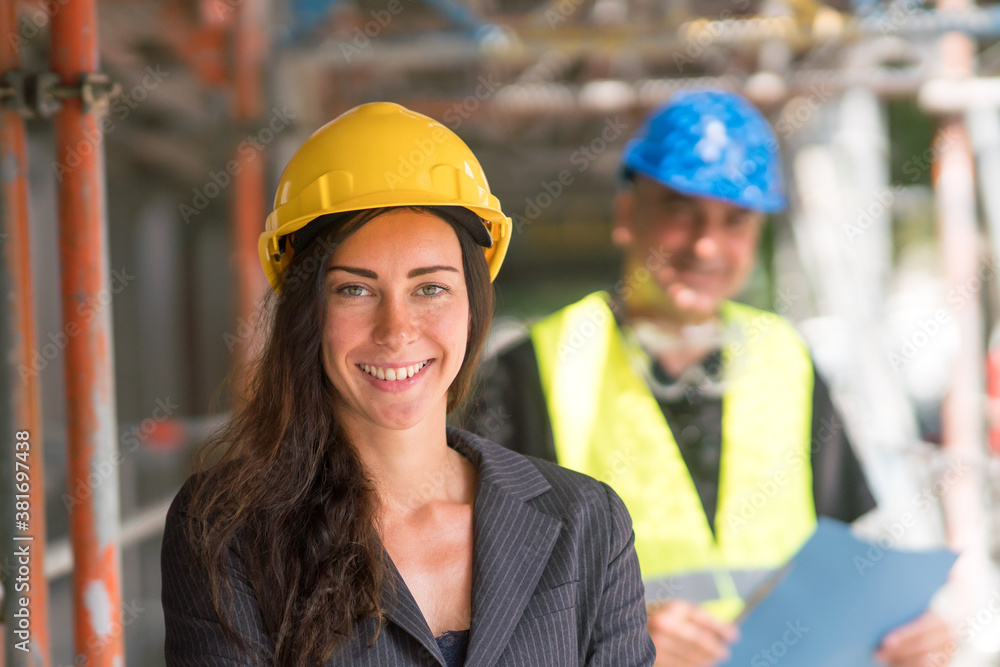 Smiling woman construction manager or engineer posing looking at the camera. On background, out of focused construction engineer Smiling woman construction manager or engineer posing looking at the camera. On background, out of focused construction engineer