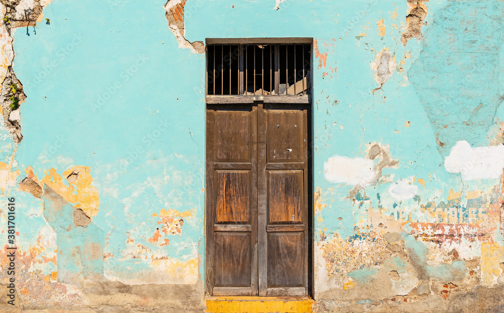 Colonial style vintage wooden door with weathered paint on facade, Antigua, Guatemala.
