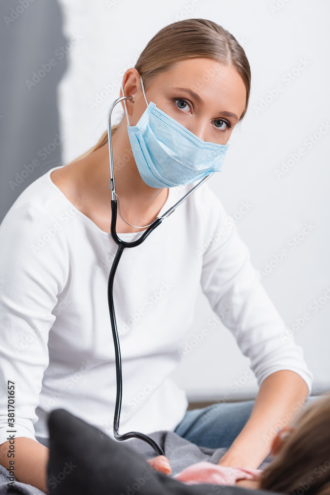 Selective focus of woman in medical mask using stethoscope near child at home Selective focus of woman in medical mask using stethoscope near child at home
