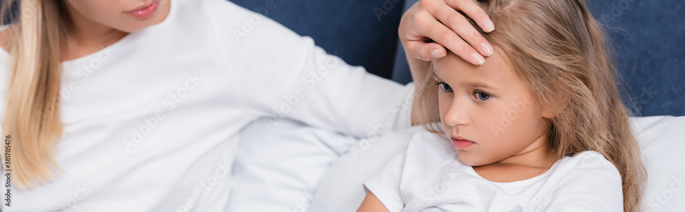 Panoramic shot of young woman touching forehead of diseased daughter on bed Panoramic shot of young woman touching forehead of diseased daughter on bed