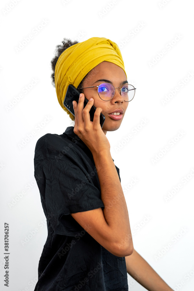 Portrait of young woman wearing glasses and yellow head scarf and speaking on mobile phone over white background Portrait of young woman wearing glasses and yellow head scarf and speaking on mobile phone over white background