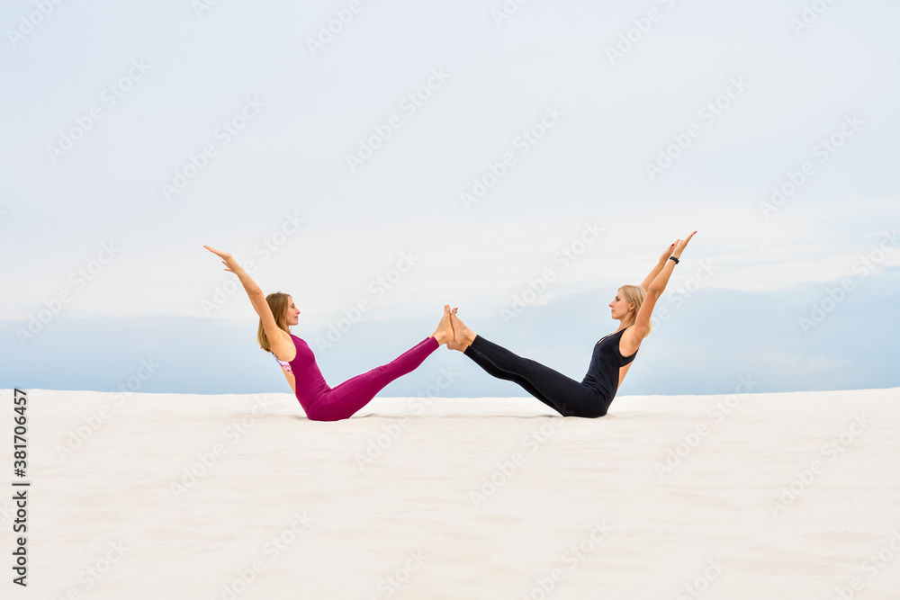 Two beautiful young women perform yoga pose navasana Two beautiful young women perform yoga pose navasana