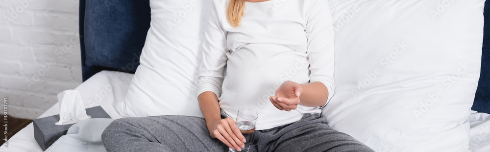 Website header of pregnant woman holding glass of water near box with napkins on bed