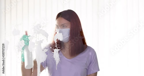 One young woman cleaning home, wiping and doing disinfection on windows, Young Woman with a face mask cleaning window at home
