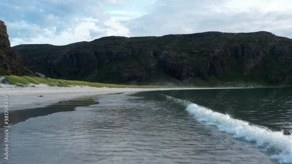 Aerial shot of northern sea (norwegian Island), clear waves are calmly hitting the white beach.