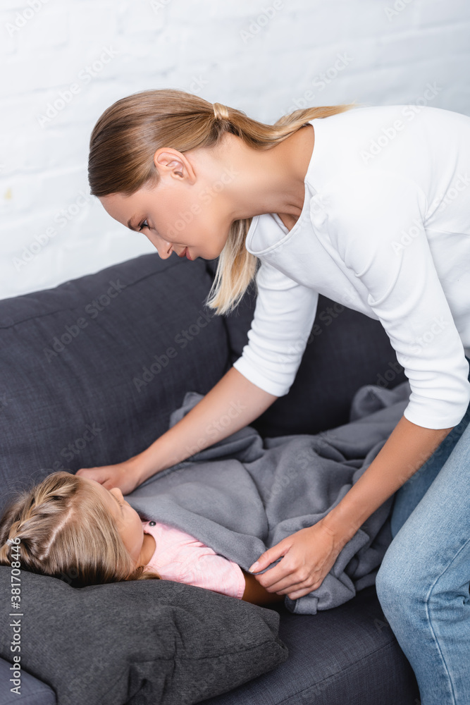 Mother covering ill daughter with blanket on couch at home Mother covering ill daughter with blanket on couch at home