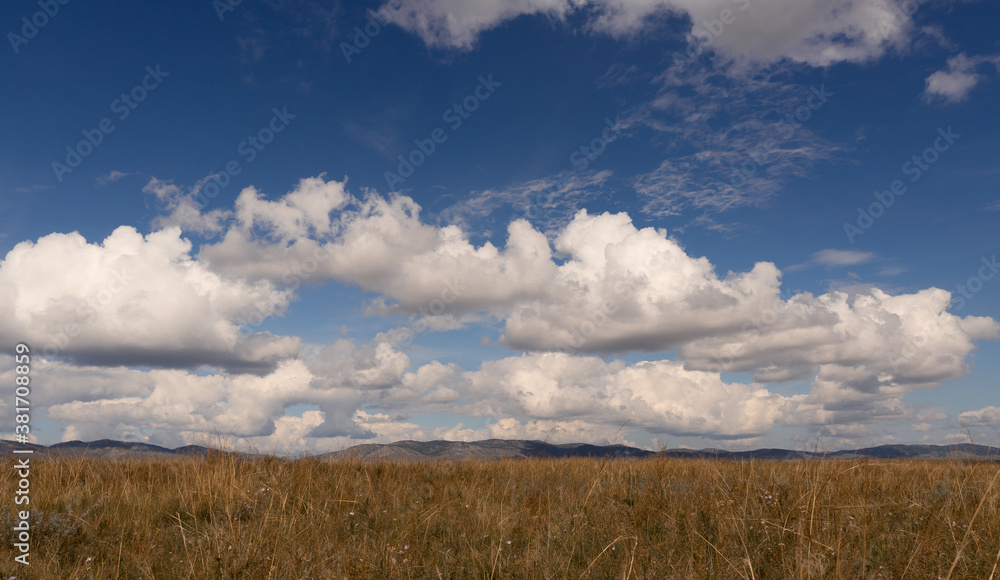 Big white clouds above the steppe meadow in Khakassia. Landscape with a grass, hills and the sky.