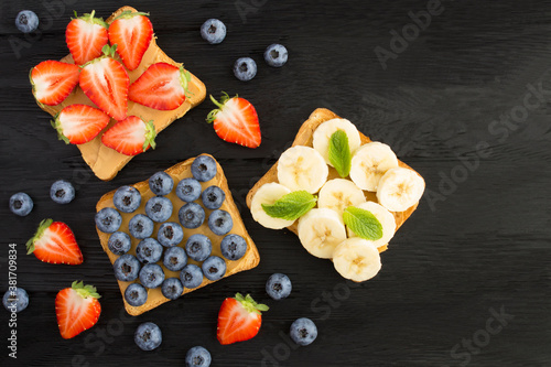 Fototapeta Naklejka Na Ścianę i Meble -  Top view of sandwiches  with peanut butter and fruit on the black wooden surface