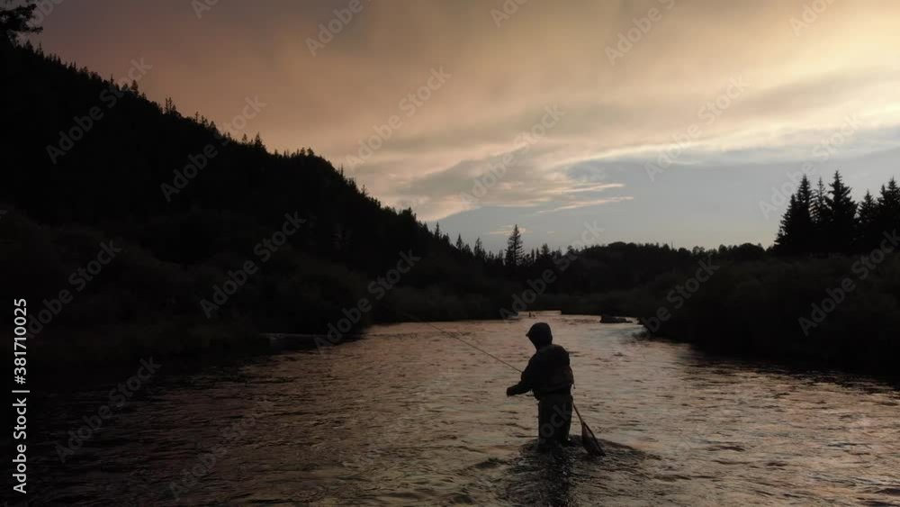 Lone fly fisherman casts his rod mid river as dusk and clouds approach Lone fly fisherman casts his rod mid river as dusk and clouds approach