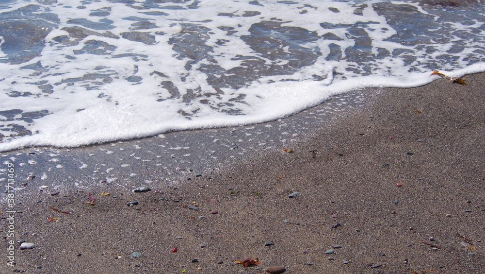 Waves reaching the shore, with sand, sea foam, small stones and seaweed Waves reaching the shore, with sand, sea foam, small stones and seaweed