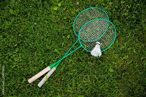 Badminton rackets and shuttlecock laying on green grass, outdoors nature background. Badminton game, sport, activity, summer, hobby, competition, tournament concept. Copy text space