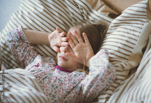 Cute little child girl waking up lying ill in bed under blanket