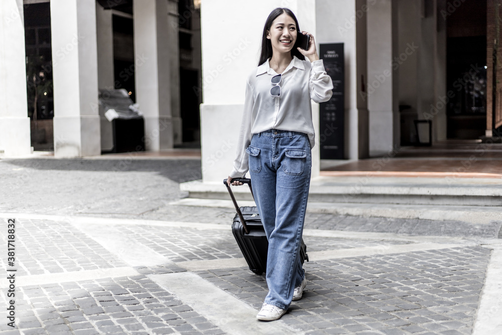 Asian woman holds a travel bag preparing to go to the accommodation and chat on the phone to a friend to meet up for a holiday party, Trolley bag, Long weekend travel, Tourism festival concept. Asian woman holds a travel bag preparing to go to the accommodation and chat on the phone to a friend to meet up for a holiday party, Trolley bag, Long weekend travel, Tourism festival concept.